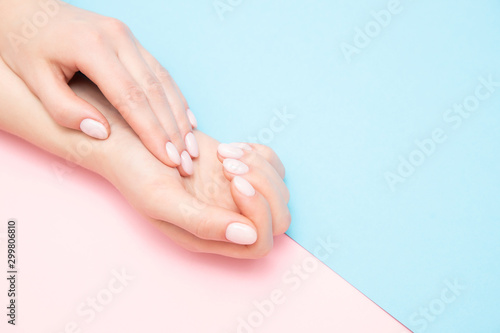 Beautiful female hands with stylish nail manicure gel polish on pink and blue background, top view. Skin care concept