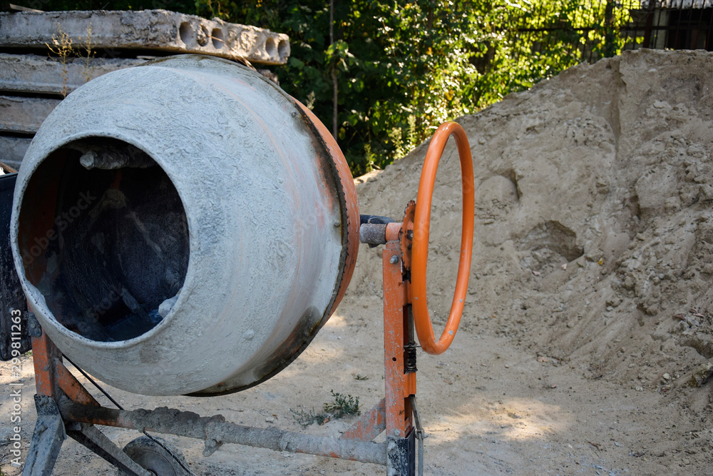Electric concrete mixer on the background of a heap of sand. Construction machinery at the production site. Electric concrete mixer on the background of a heap of sand. Construction machinery at the production site.