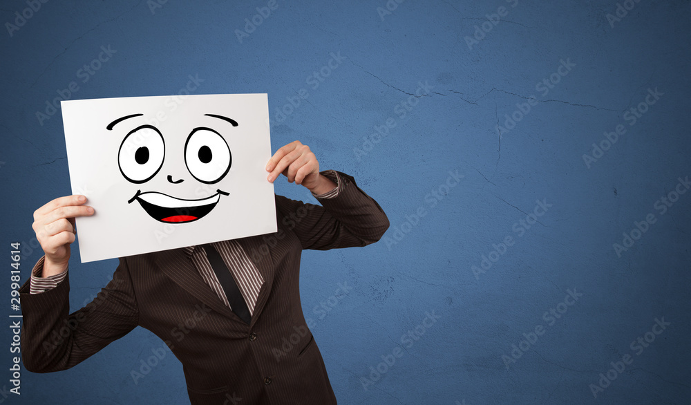 Young student holding a paper with laughing emoticon in front of his face Young student holding a paper with laughing emoticon in front of his face