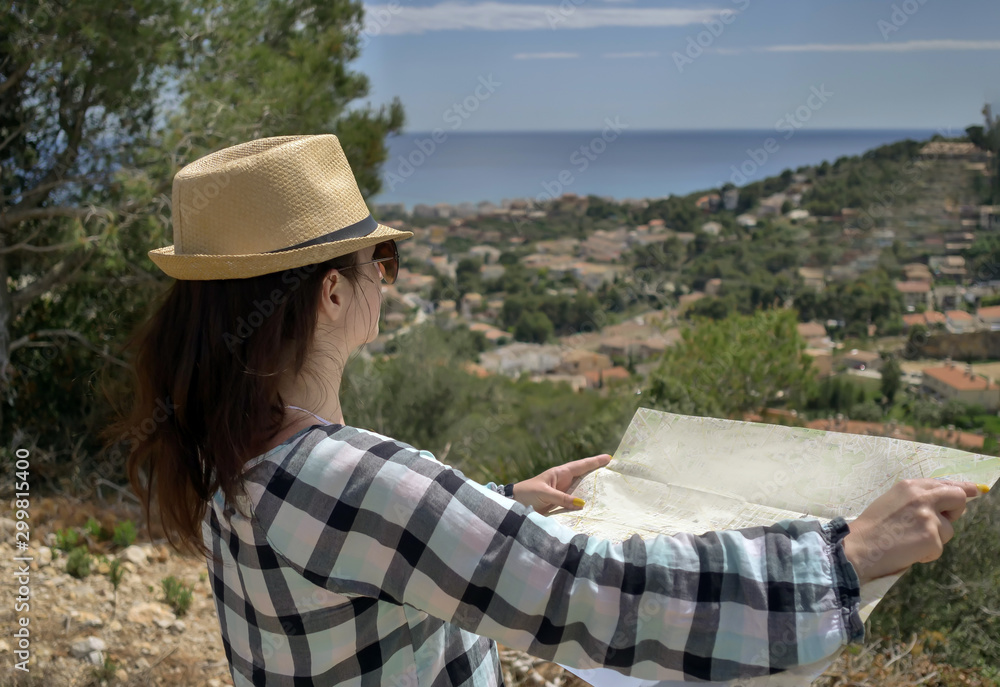 Brunette girl in a hat stands on a mountain holds a map of the area in her hands, copyspace