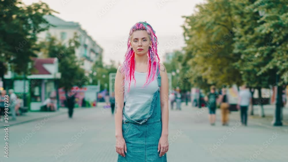 Time lapse portrait of beautiful hipster girl with bright hair and tattoo outside in pedestrian street looking at camera. Youth culture, stylish people and city concept. Time lapse portrait of beautiful hipster girl with bright hair and tattoo outside in pedestrian street looking at camera. Youth culture, stylish people and city concept.
