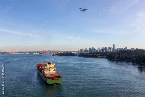 Vancouver, British Columbia, Canada. Aerial View from Above of a Cargo Ship arriving to the Port with Downtown City in the Background during a sunny evening.