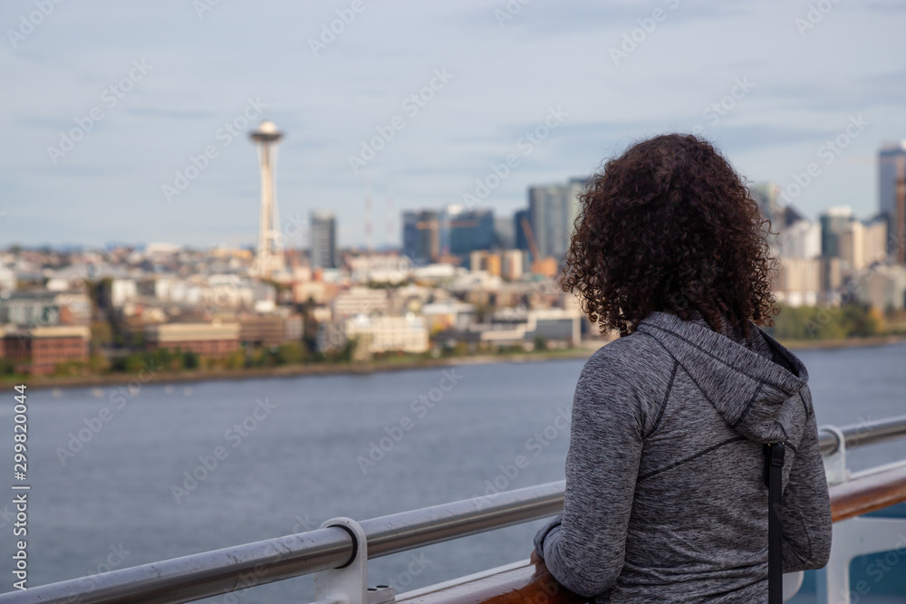 Downtown Seattle, Washington, United States of America. Girl on a Cruise Ship is enjoying the View of the Modern City on the Pacific Ocean Coast during a sunny and cloudy Autumn evening. Downtown Seattle, Washington, United States of America. Girl on a Cruise Ship is enjoying the View of the Modern City on the Pacific Ocean Coast during a sunny and cloudy Autumn evening.