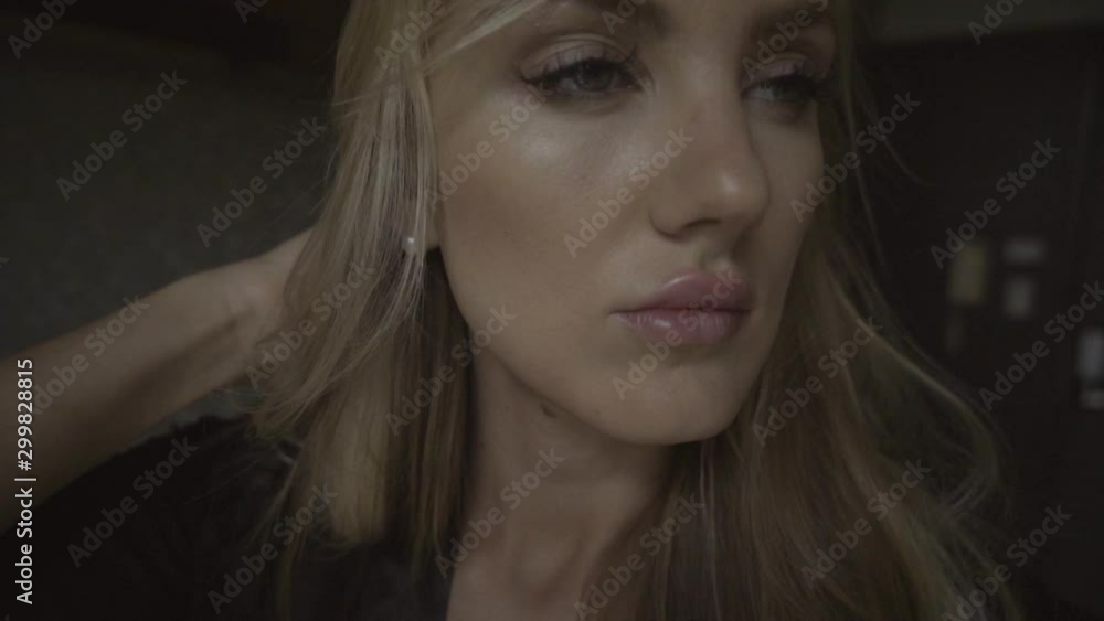 Close up view on face of young sensual woman standing and correcting blonde hair in modern apartment. Pensive girl looking in window in stylish interior. Close up view on face of young sensual woman standing and correcting blonde hair in modern apartment. Pensive girl looking in window in stylish interior.