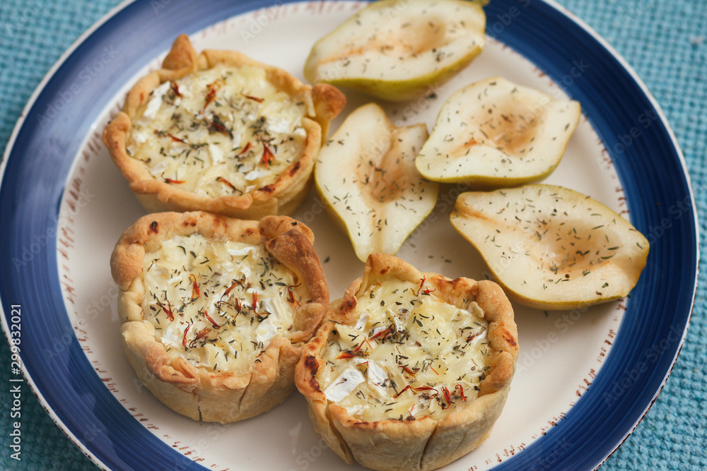 Puff pastry julienne with mushrooms and camembert cheese. Sliced sweet pear. White decorative plate with blue border. Traditional cuisine. Tapas. Puff pastry julienne with mushrooms and camembert cheese. Sliced sweet pear. White decorative plate with blue border. Traditional cuisine. Tapas.