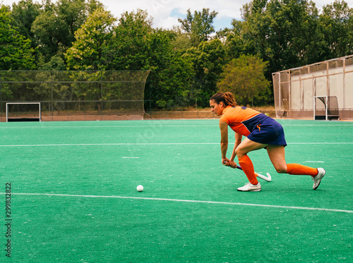 Female hockey player attacking and hitting on a grass field.