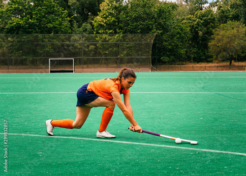Female hockey player attacking and hitting on a grass field.