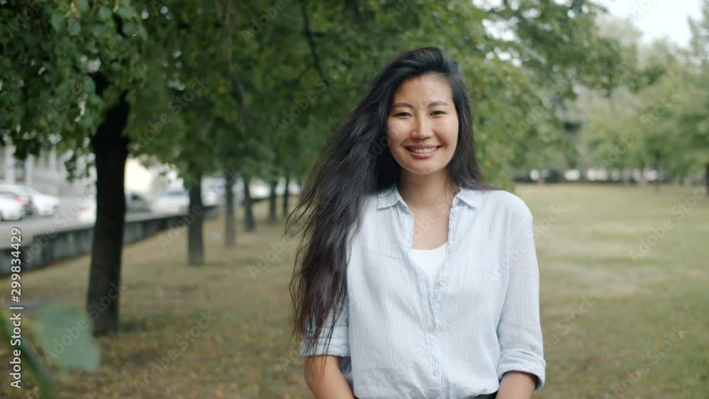 Portrait of attractive Asian woman smiling standing in green park alone in summer looking at camera with cheerful face. Happiness and beautiful nature concept. Portrait of attractive Asian woman smiling standing in green park alone in summer looking at camera with cheerful face. Happiness and beautiful nature concept.