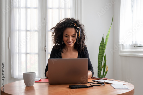 Shot of young latin woman working at home with laptop and documents
