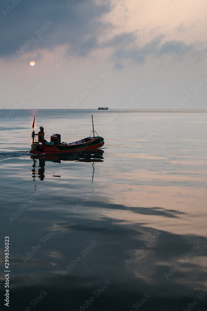 Man in a small boat heading out to sea at dawn, Koh Rong island, Cambodia. Dramatic sky and calm sea.