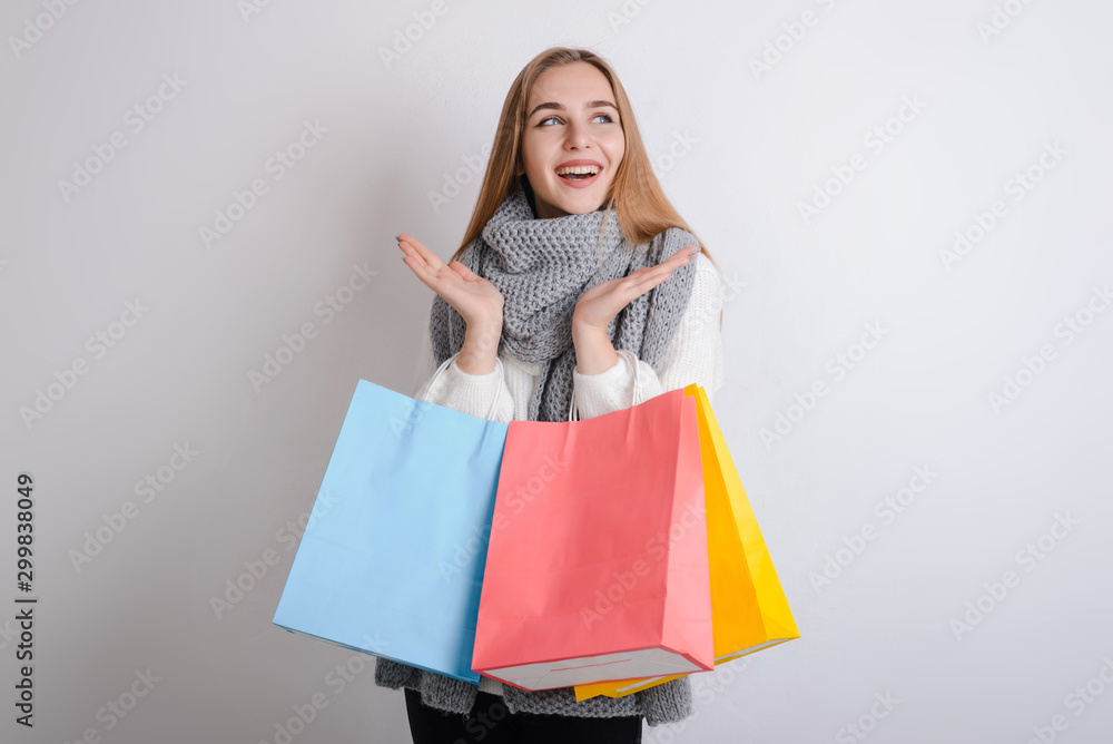 Excited beautiful girl wearing warm sweater and scarf holding shopping bags isolated over gray background