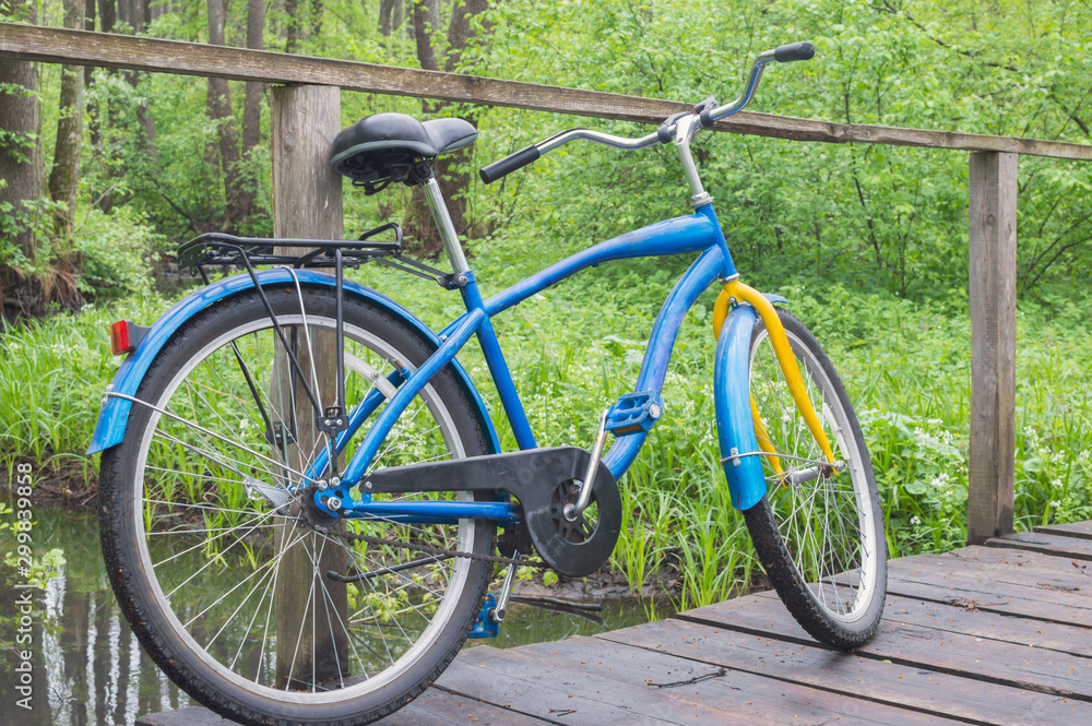 A bicycle is parked on an old wooden bridge by a forest stream. Soft selective focus