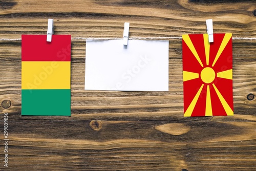 Hanging flags of Guinea and Macedonia attached to rope with clothes pins with copy space on white note paper on wooden background.Diplomatic relations between countries.