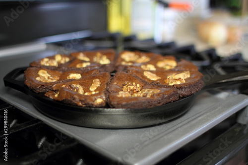 Chocolate brownies with walnuts baked in a cast iron wedge pan, resting on the stove top in a home kitchen.