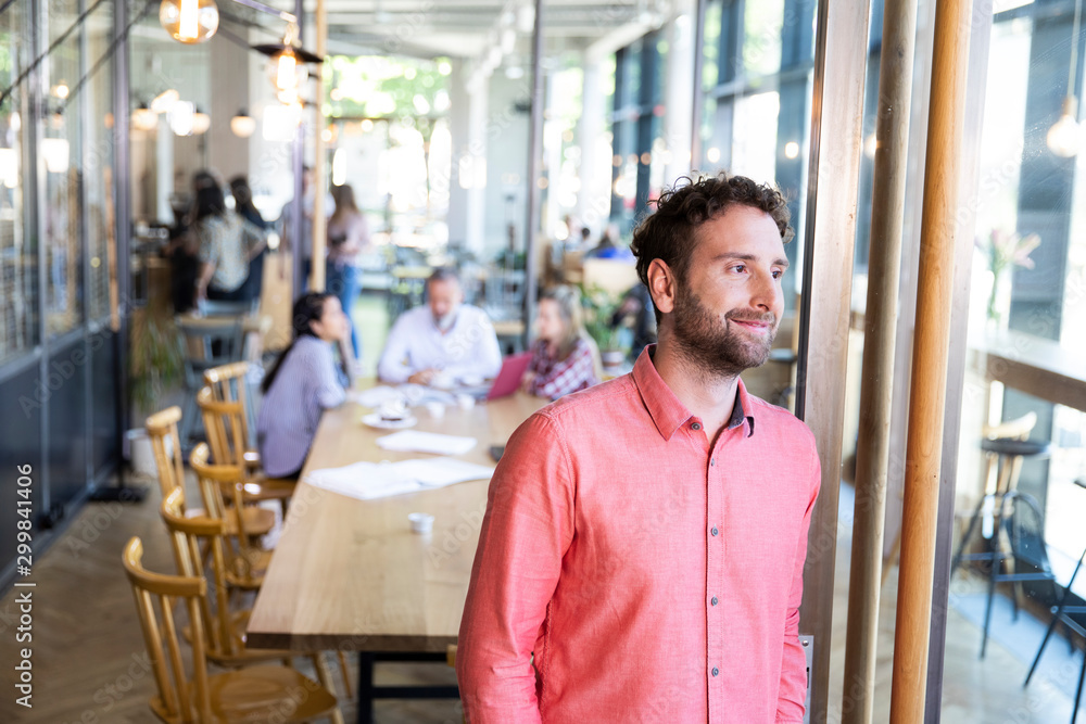 Portrait of casual businessman in a cafe with colleagues having a meeting in background Portrait of casual businessman in a cafe with colleagues having a meeting in background