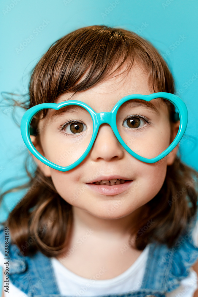 Portrait of cute little girl with heart shaped glasses on blue background Portrait of cute little girl with heart shaped glasses on blue background