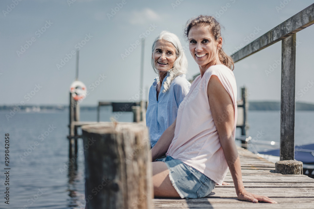 Mother and daughter sitting on jetty, relaxing at the sea Mother and daughter sitting on jetty, relaxing at the sea