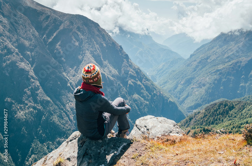 Young hiker backpacker sitting on the peak edge and enjoying mountains view valley during high altitude Everest Base Camp (EBC) trekking route near Phortse, Nepal. Active vacations concept image. photo