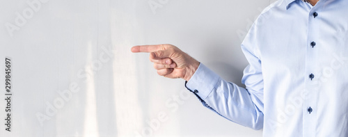 A man in a blue shirt shows a direction with his finger. Direction indication, forefinger and gray background.