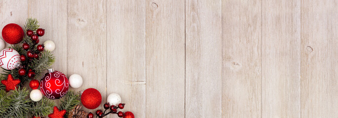 Christmas corner border banner with red and white ornaments and branches. Overhead view on a rustic gray wood background with copy space.