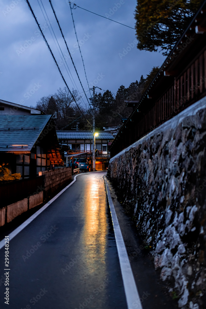 Gifu prefecture town in Takayama, Japan in early spring in traditional village at night with illuminated lantern lamp and stone wall by road