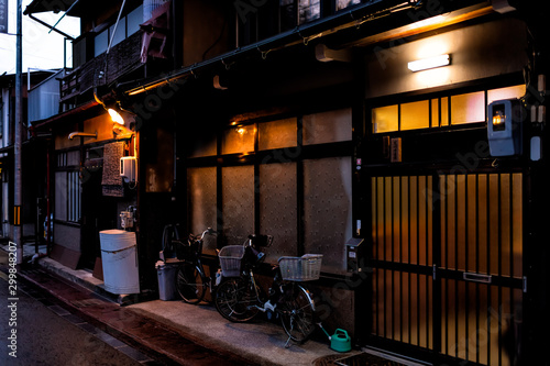 Fototapeta Naklejka Na Ścianę i Meble -  Takayama, Japan empty street at night with illuminated house and road in Gifu Prefecture with parked traditional bicycles and basket