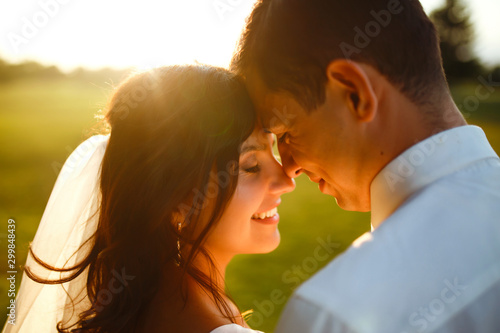 Lovely wedding couple at sunset. Bride and groom in wedding attire with a bouquet of flowers is in the hands against the backdrop of the  green field at sunset. Romantic Married young family. 