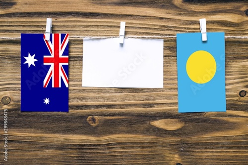 Hanging flags of Heard and Mcdonald Islands and Palau attached to rope with clothes pins with copy space on white note paper on wooden background.Diplomatic relations between countries. photo