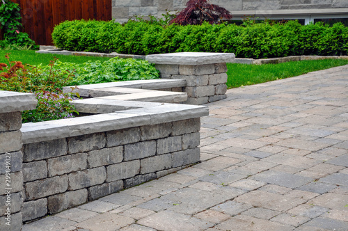 A seat wall with pillars and natural stone coping helps define a tumbled paver driveway and is a beautiful landscaping feature. photo