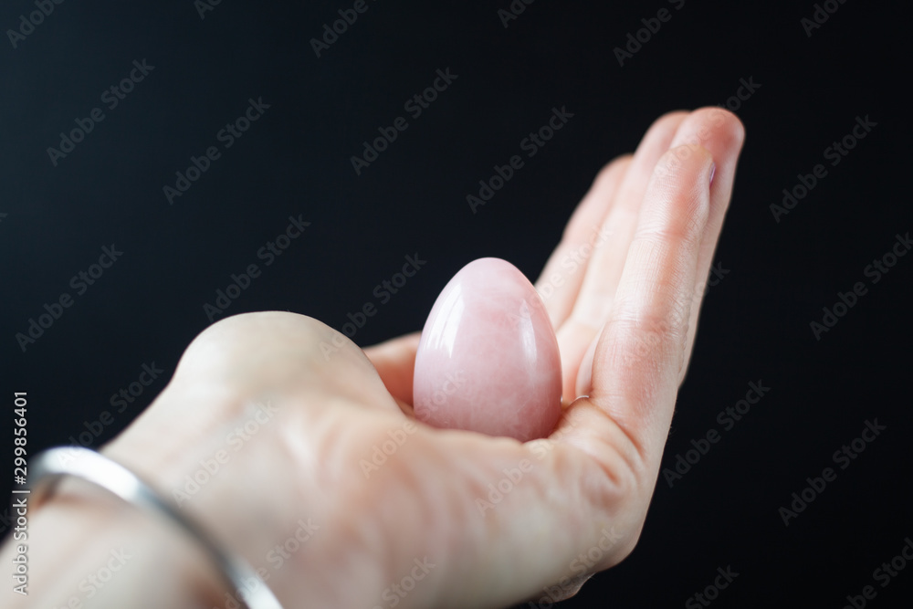 woman holding in hand a vaginal (yoni) egg. Rose quartz crystal jade egg. Copy space