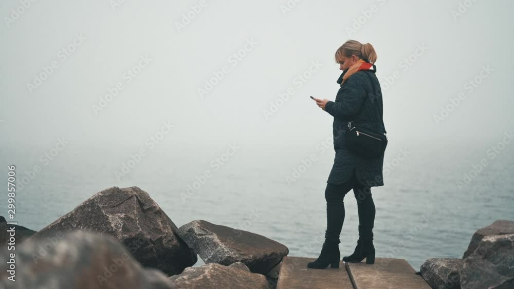 Full length portrait of woman using smart phone standing outside in the cold