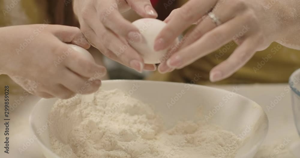 Extreme close-up of plate with white flour. Adult female Caucasian hands breaking egg, little girl smashing another egg. Small helper assisting mom in cooking. Cinema 4k footage ProRes HQ. Extreme close-up of plate with white flour. Adult female Caucasian hands breaking egg, little girl smashing another egg. Small helper assisting mom in cooking. Cinema 4k footage ProRes HQ.