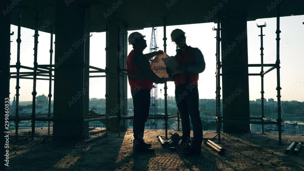 Constructions planning held by two construction engineers at the building lot