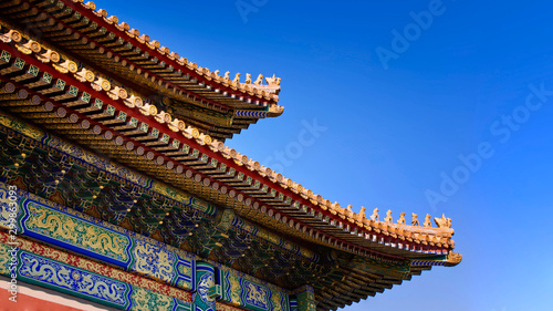 curved roofs in traditional Chinese style with figures on the blue sky background. The Imperial Palace in Beijing © Alena Charykova
