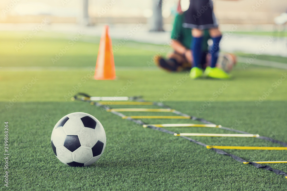 Soccer ball and ladder drills on green artificial turf with blurry kid football player and coach are training. Soccer training or football training equipment in academy.