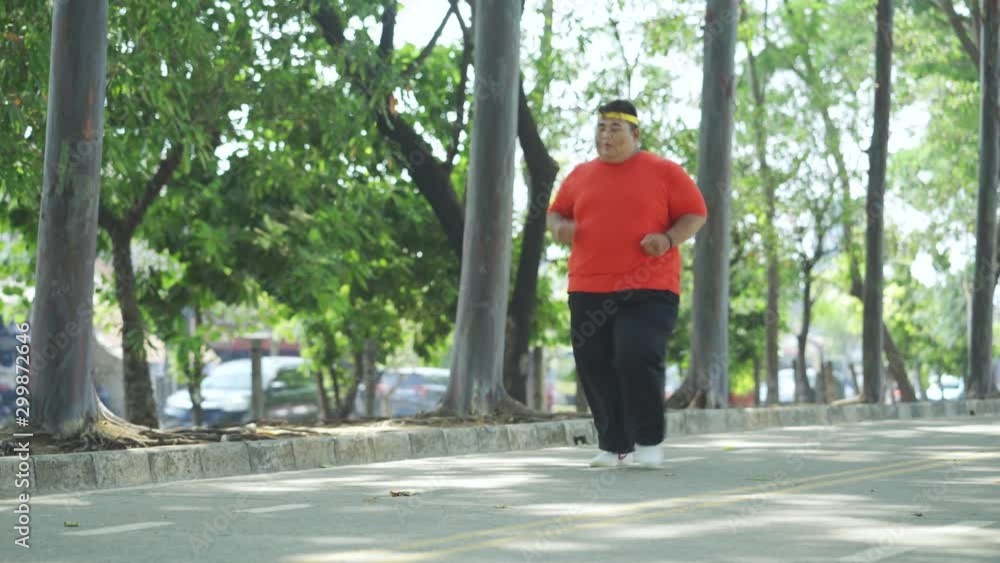 JAKARTA, Indonesia - October 28, 2019: Obese man running at park and taking a rest by sitting on the road under green trees. Shot in 4k resolution JAKARTA, Indonesia - October 28, 2019: Obese man running at park and taking a rest by sitting on the road under green trees. Shot in 4k resolution