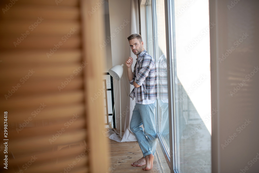 Handsome young man standing near window at the weekend Handsome young man standing near window at the weekend