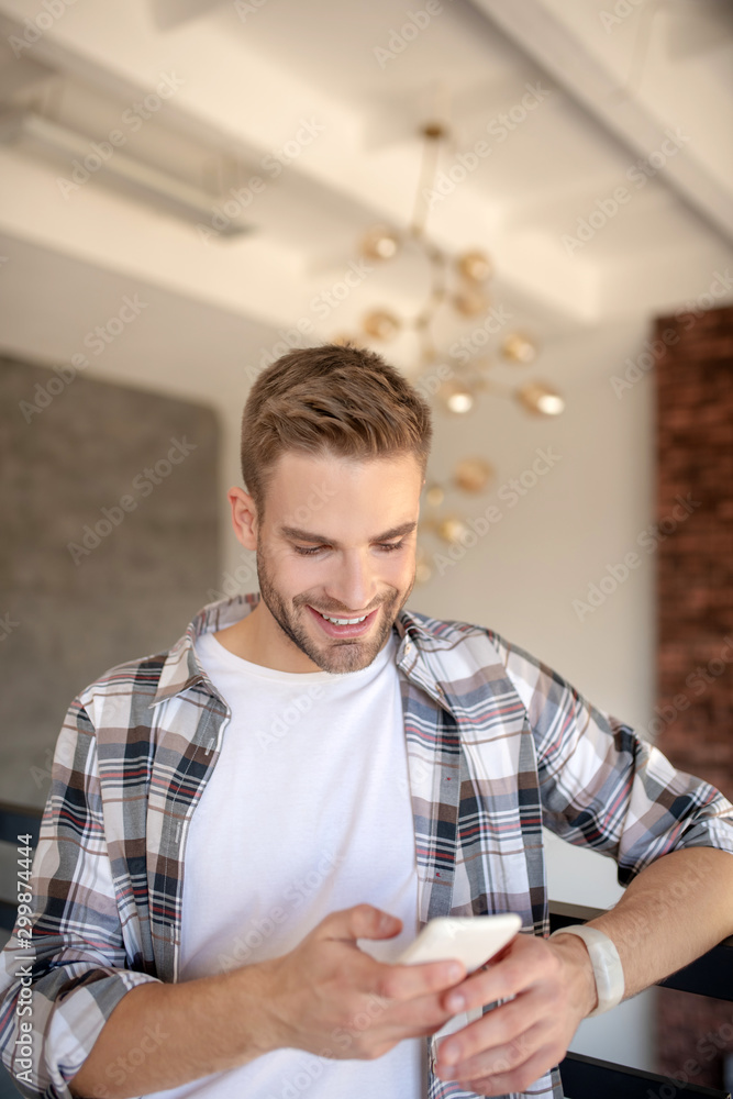Obraz premium Handsome man smiling while reading message from girlfriend