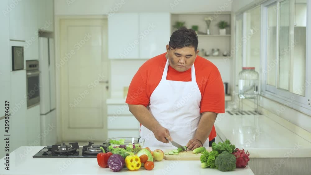 Overweight young man slicing fresh vegetables to make salad for dieting menu. Shot in 4k resolution Overweight young man slicing fresh vegetables to make salad for dieting menu. Shot in 4k resolution