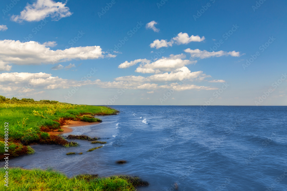 The shore of a large lake, against a background of blue sky and white clouds.