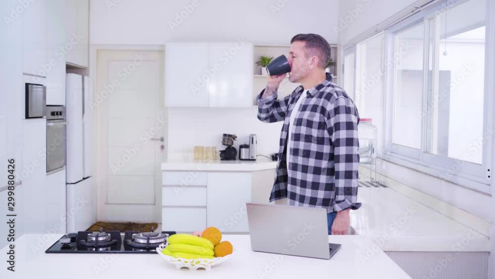 Handsome caucasian man drinking coffee and using laptop on the morning in the kitchen at home. Shot in 4k resolution Handsome caucasian man drinking coffee and using laptop on the morning in the kitchen at home. Shot in 4k resolution
