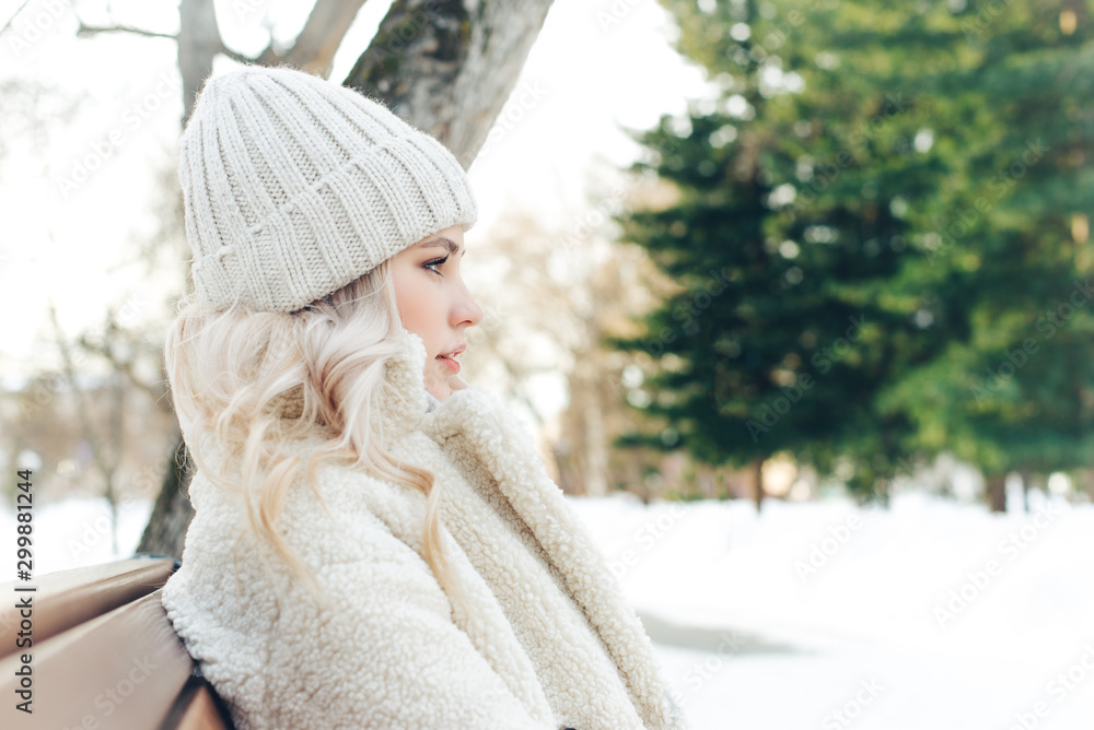 Young beautiful blonde girl sits on a bench in the park in winter Young beautiful blonde girl sits on a bench in the park in winter