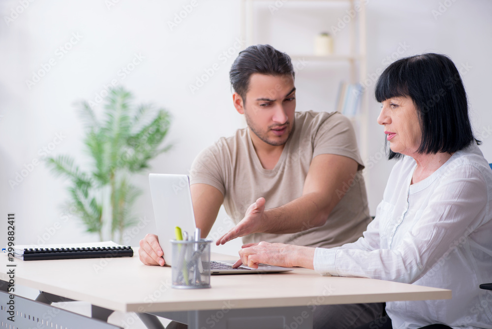 Fototapeta premium Young male employee explaining to old female colleague how to us