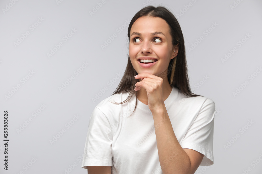Attractive positive woman looking aside and dreaming. Pleased smiling female thinking with dreamy expression, isolated on gray background Attractive positive woman looking aside and dreaming. Pleased smiling female thinking with dreamy expression, isolated on gray background