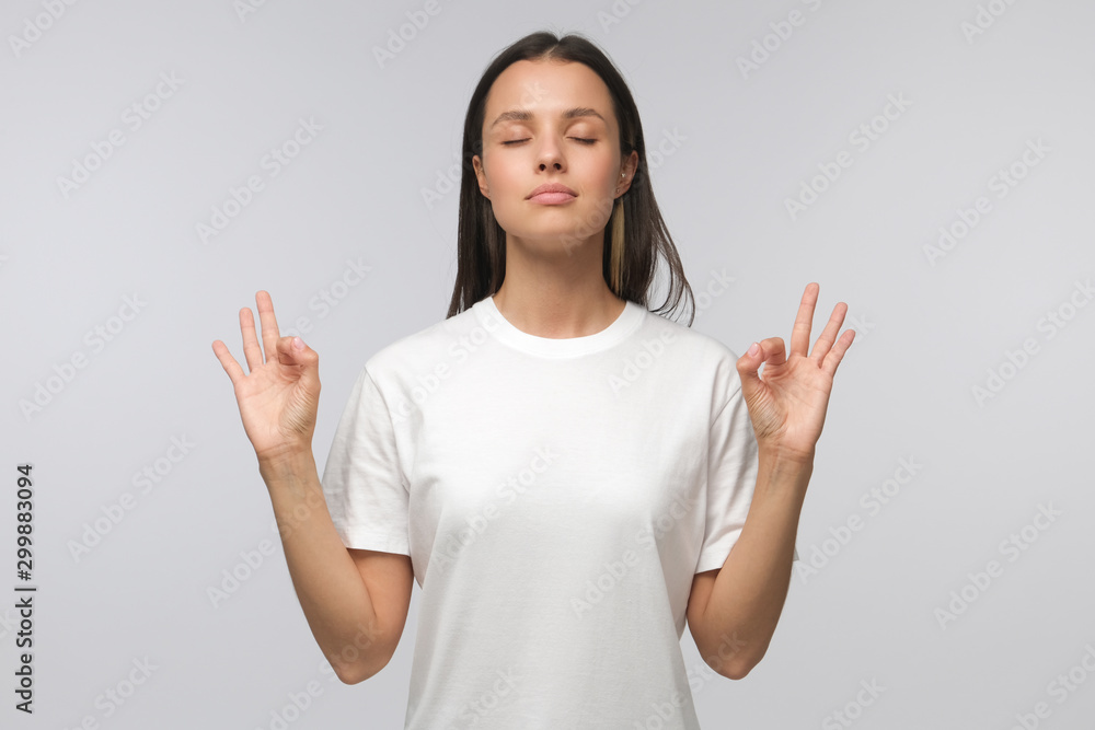 Yoga and meditation concept. Concentrated relaxed woman standing with closed eyes, having relaxation while meditating, trying to find balance and harmony isolated on gray Yoga and meditation concept. Concentrated relaxed woman standing with closed eyes, having relaxation while meditating, trying to find balance and harmony isolated on gray