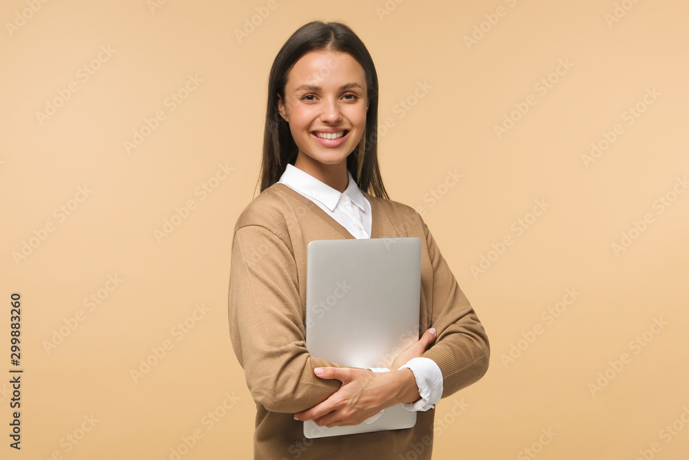 Female college student smiling at camera, holding laptop ready to go to studies, isolated on brown background Female college student smiling at camera, holding laptop ready to go to studies, isolated on brown background