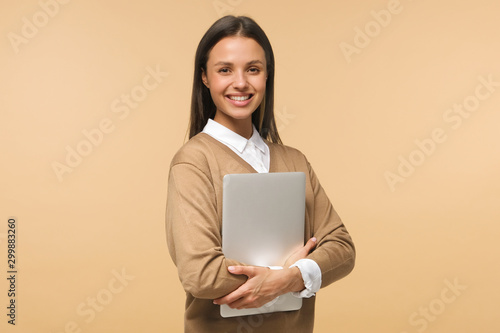 Female college student smiling at camera, holding laptop ready to go to studies, isolated on brown background