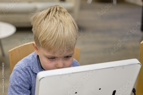 Wallpaper Mural Elementary school boy sitting in library, using touchscreen computer for education. Concentrated and tired Torontodigital.ca