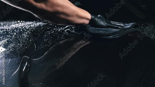 Using rag in palm of your hand, drops are removed from the car. Drop flow down the hood. Close up view of bonnet car. Polishing and washing auto.