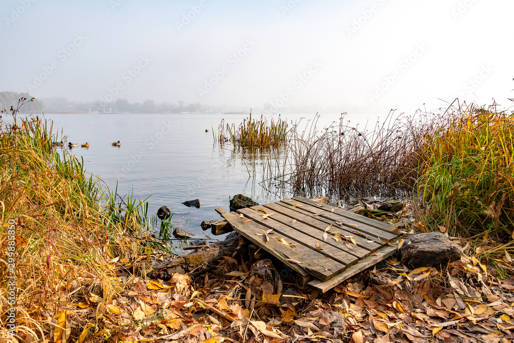 A wooden pontoon over big stones close to the blue Dnieper river is waiting for the fisherman.